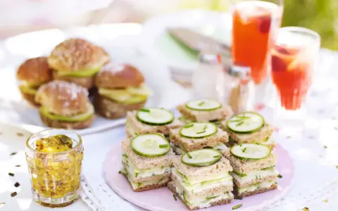 Små smörgåsar med gurka och ost, perfekta för ett afternoon tea recept. Serveras med röda drycker och senap.