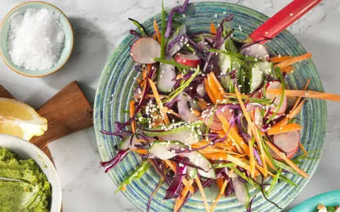 En fräsch asiatisk kålsallad med strimlad morot, rödkål, gurka och rädisor, toppad med sesamfrön.