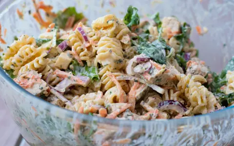 En stor skål med krämig pastasallad med kyckling, morötter, rödlök och gröna blad. Perfekt för en somrig picknick.