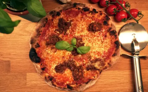 En härlig napolitansk pizza med köttfärs och basilika, redo att skäras med pizzaskäraren.