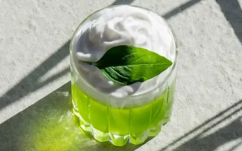En uppfriskande grön drink med fluffigt kokosskum och ett grönt blad som dekoration. Perfekt för en solig dag.