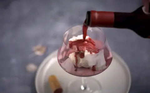En flaska häller upp rött dessertvin till glass i ett glas. En perfekt kombination för en lyxig efterrätt.