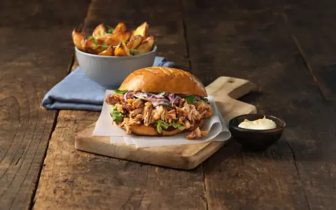 En saftig pulled pork burgare med krispig kål och en skål med ugnsrostade potatisklyftor.