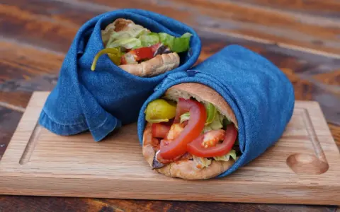 Två kebabrullar inslagna i jeans på en träbricka. Ett enkelt kebab recept med färska grönsaker.