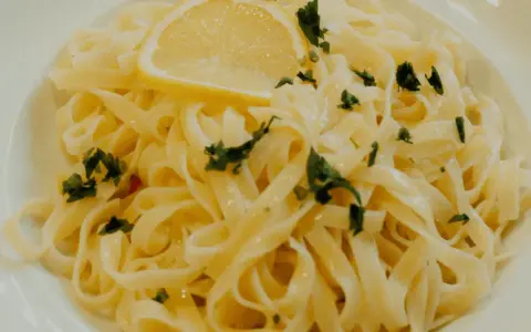 En tallrik med krämig citronpasta, toppad med en citronskiva och färsk persilja. Perfekt för en lätt lunch eller middag.