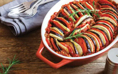 En vackert upplagd ratatouille i en ugnsform, perfekt för en nyttig middag. Grönsakerna är skivade och arrangerade i ett mönster, toppad med rosmarin.