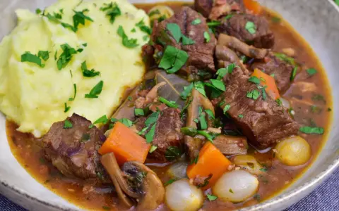 En mustig boeuf bourguignon med möra köttbitar, champinjoner, morötter och små lökar, serverad med krämigt potatismos.