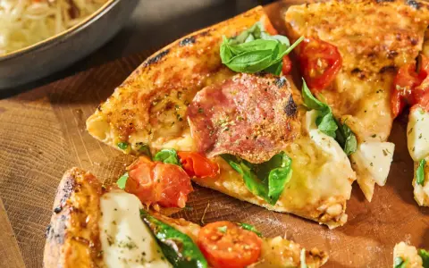 Fredriks fika: Krispig pizzadeg med salami, tomater och färsk basilika på en träskärbräda.
