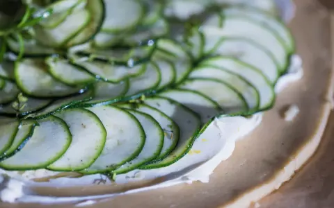 Tunna skivor av zucchini läggs på en krämig fyllning på en pajdeg. En underbart god paj som snart är redo att avnjutas.