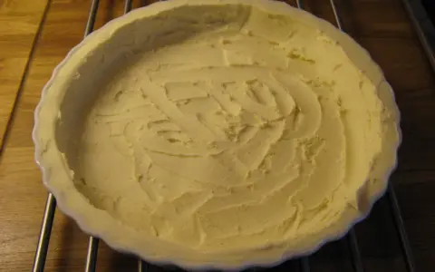 En vit pajform med en färdig glutenfri pajdeg från Lailas. Pajdegen är pressad mot formens kanter och har ett mönster i mitten.