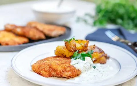 En tallrik med krispig panerad kyckling, rostade potatisklyftor och en krämig dillsås. En klassisk svensk rätt som ser utsökt ut.