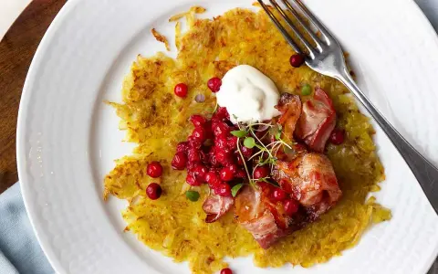 En gyllene råraka med knaperstekt bacon, lingon och en klick gräddfil. Ett klassiskt råraka recept som är perfekt för en helgmåltid.