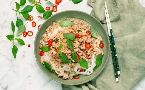En skål med nudlar och köttfärs, toppad med färsk basilika och chili. En härlig thai mat som ser utsökt ut.