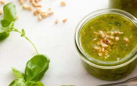 Färska basilikablad och pinjenötter bredvid en burk med hemlagad pesto genovese recept.