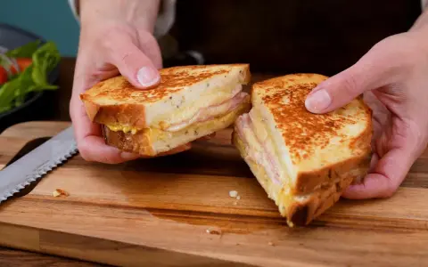 En gyllene croque monsieur, perfekt rostad och fylld med ost och skinka, delas på ett skärbräde.