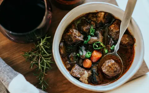 En skål med mustig boeuf bourguignon, perfekt för ett mysigt recept. Serveras med en sked och en kvist rosmarin.