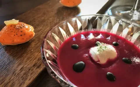 En vacker rödbetssoppa med en klick gräddfil och svarta droppar, perfekt mat till chablis. Bredvid ligger en orange aptitretare.