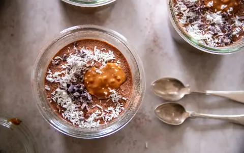 Chokladpudding med kokosflingor och kakaonibs, en perfekt proteinrik frukost. Två skedar ligger bredvid.