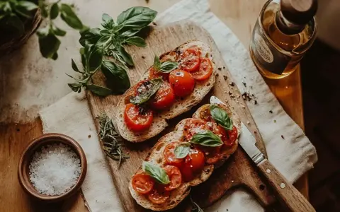 Två skivor rostat bröd med tomater och basilika, redo att avnjutas som ett enkelt bruschetta recept. En flaska olivolja och en skål flingsalt finns i närheten.
