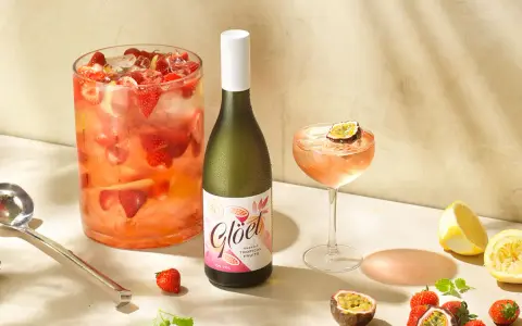 En flaska vitt vin står bredvid en drink med passionsfrukt och jordgubbar. Perfekt för att drink vitt vin en solig dag.