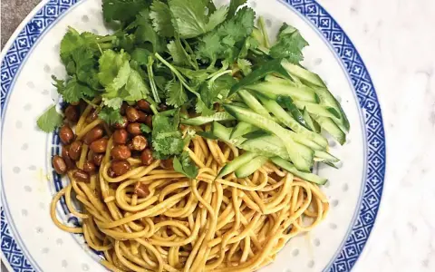 En läcker asiatisk nudelsallad med krispig gurka, rostade jordnötter och färsk koriander på en vackert mönstrad tallrik.