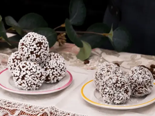 Fredriks fika: de godaste chokladbollar, rullade i kokos och pärlsocker, serverade på små fat med en grönskande bakgrund.