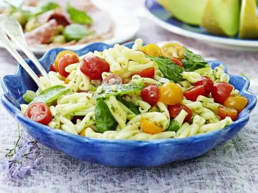 En härlig italiensk pastasallad med körsbärstomater och basilika i en blå skål, perfekt för en sommarlunch.
