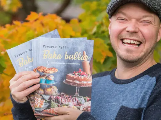 Fredrik Nylen håller upp sina böcker om kanelbullar med kardemumma, perfekt för Fredriks fika.