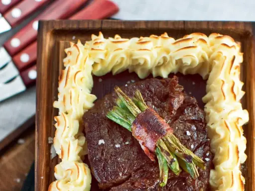 En saftig biff med sparris inslagen i bacon, omgiven av krispig potatispuré. Ett perfekt plankstek recept för en festmåltid.