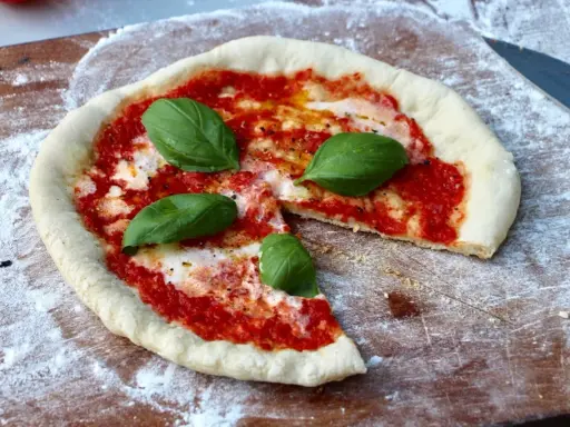 En nybakad pizza på grillen, med tomatsås, mozzarella och färsk basilika, redo att avnjutas.