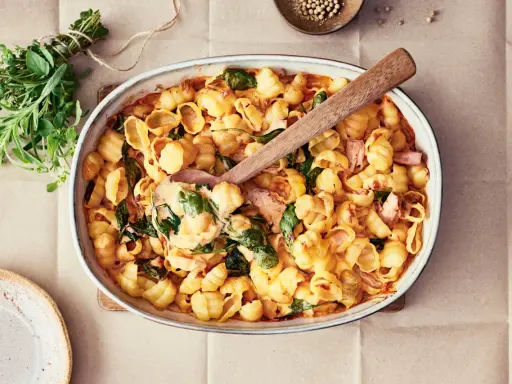 Enkel lyxig middag: krämig pastasås med snäckpasta, spenat och skinka i ugnsform. Serveras med färska örter.