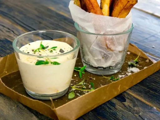 En krämig creme fraiche sås med örter, serverad bredvid en glasburk med pommes frites på ett rustikt träbord.