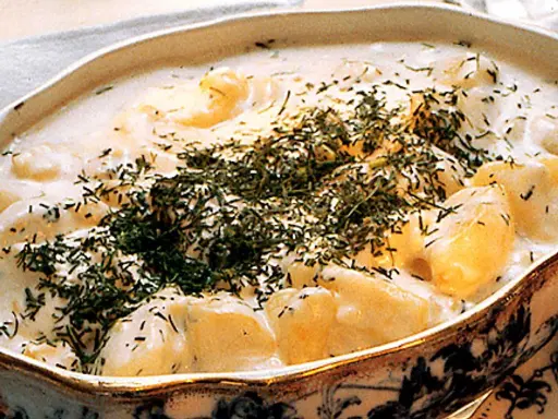 En krämig stuvad potatis med dill, serverad i ett vackert uppläggningsfat.