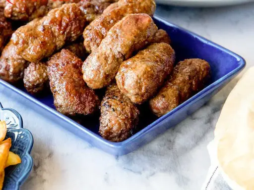 En blå skål fylld med saftiga cevapcici, redo att avnjutas. Ett perfekt cevapcici recept för alla köttälskare.