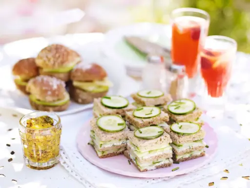 Små smörgåsar med gurka och ost, perfekta för ett afternoon tea recept. Serveras med röda drycker och senap.