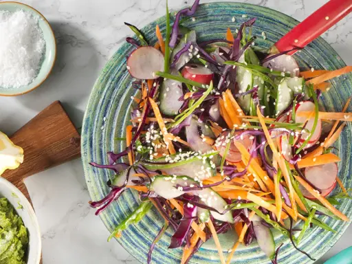 En fräsch asiatisk kålsallad med strimlad morot, rödkål, gurka och rädisor, toppad med sesamfrön.