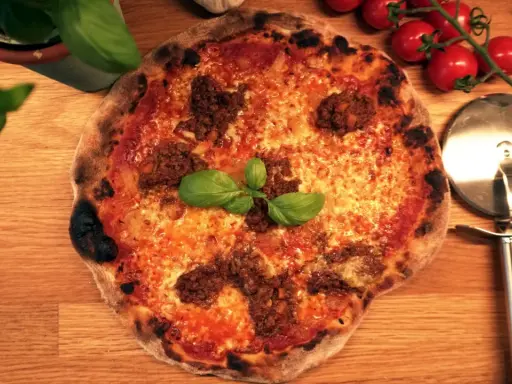 En härlig napolitansk pizza med köttfärs och basilika, redo att skäras med pizzaskäraren.