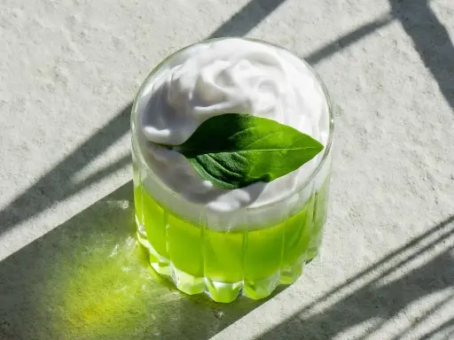 En uppfriskande grön drink med fluffigt kokosskum och ett grönt blad som dekoration. Perfekt för en solig dag.