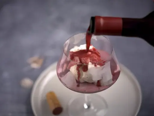 En flaska häller upp rött dessertvin till glass i ett glas. En perfekt kombination för en lyxig efterrätt.