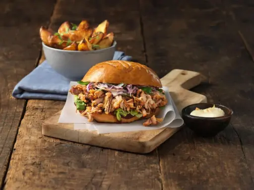 En saftig pulled pork burgare med krispig kål och en skål med ugnsrostade potatisklyftor.