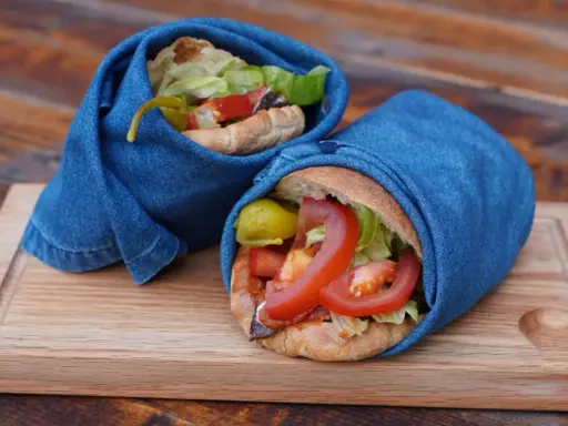 Två kebabrullar inslagna i jeans på en träbricka. Ett enkelt kebab recept med färska grönsaker.