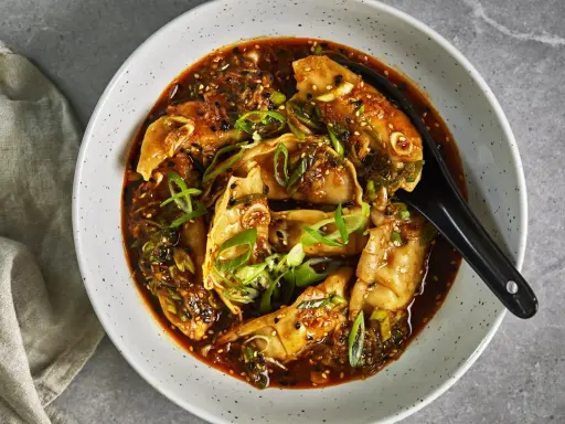En skål med dumplings i en kryddig sås, toppad med salladslök och sesamfrön. Ett perfekt lunch recept för en smakrik måltid.