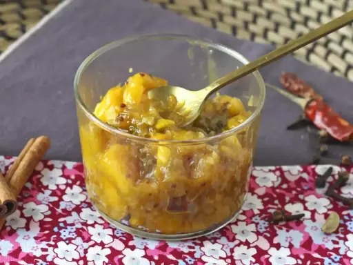 En skål med gyllene mango chutney, perfekt för ditt mango chutney recept. Kryddor som kanel och chili ligger bredvid.