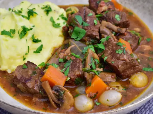 En mustig boeuf bourguignon med möra köttbitar, champinjoner, morötter och små lökar, serverad med krämigt potatismos.