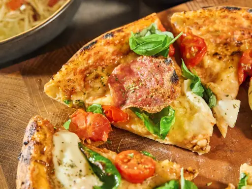 Fredriks fika: Krispig pizzadeg med salami, tomater och färsk basilika på en träskärbräda.