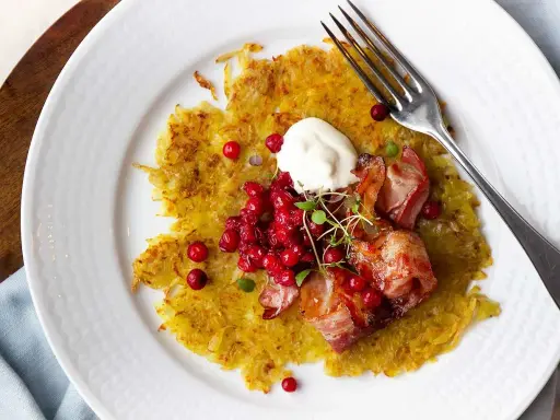 En gyllene råraka med knaperstekt bacon, lingon och en klick gräddfil. Ett klassiskt råraka recept som är perfekt för en helgmåltid.