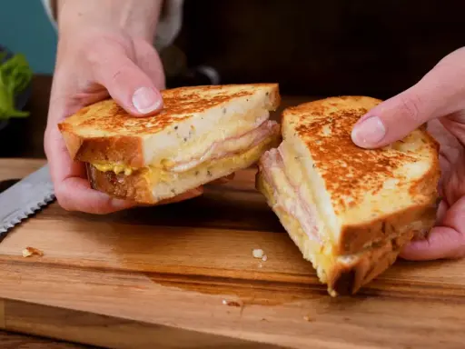 En gyllene croque monsieur, perfekt rostad och fylld med ost och skinka, delas på ett skärbräde.