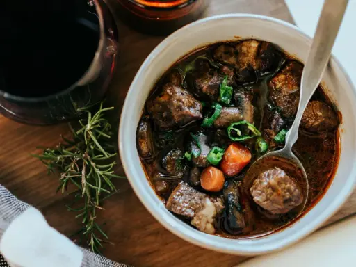 En skål med mustig boeuf bourguignon, perfekt för ett mysigt recept. Serveras med en sked och en kvist rosmarin.