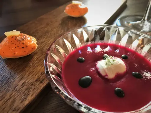 En vacker rödbetssoppa med en klick gräddfil och svarta droppar, perfekt mat till chablis. Bredvid ligger en orange aptitretare.