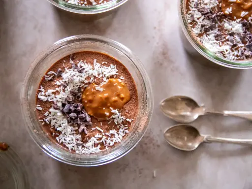 Chokladpudding med kokosflingor och kakaonibs, en perfekt proteinrik frukost. Två skedar ligger bredvid.